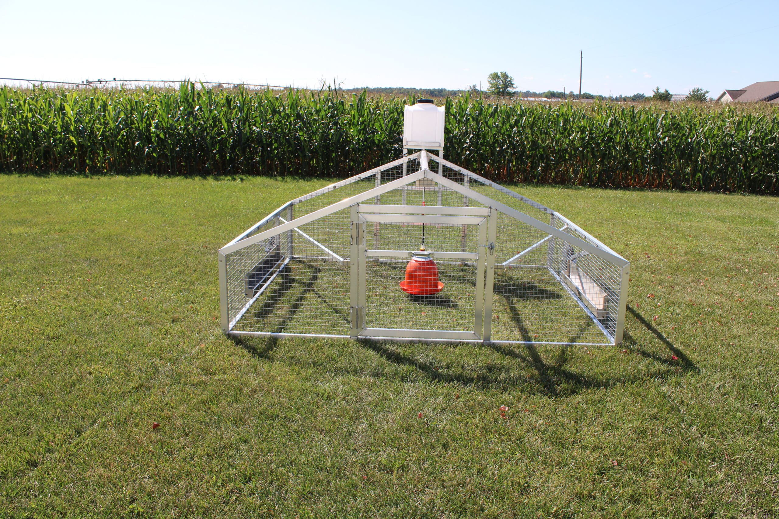 mobile chicken coop with heat lamp in grass by cornfield